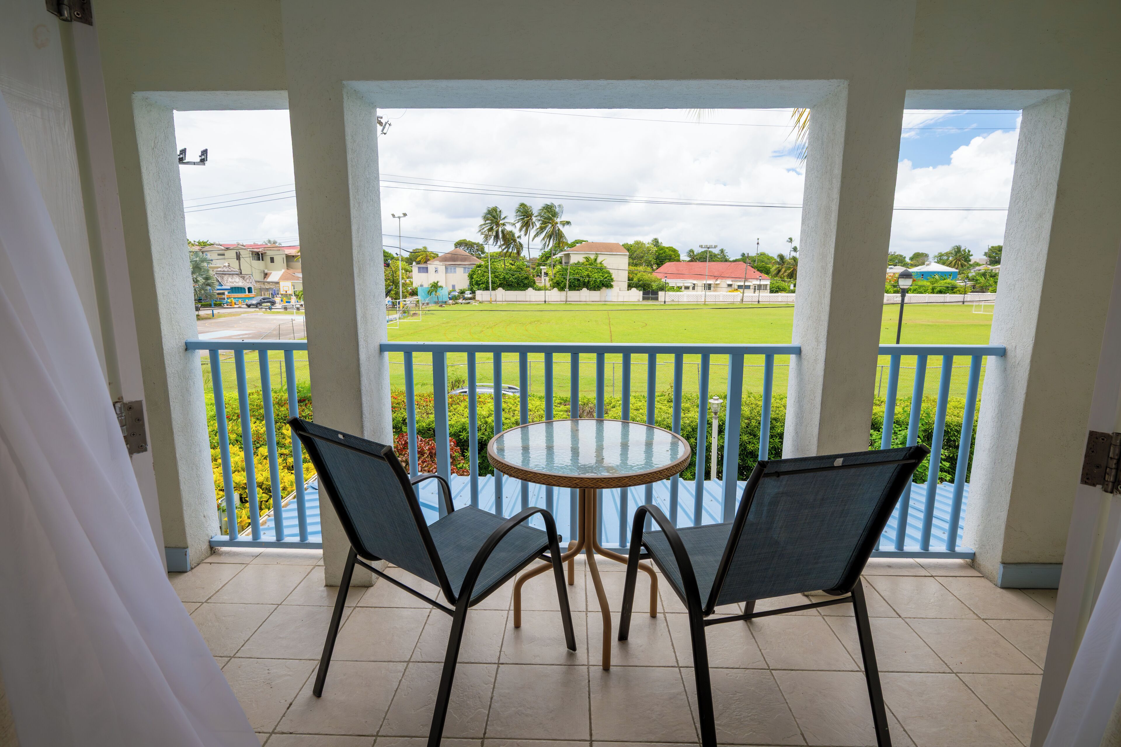 A balcony with a round table and two chairs, overlooking a green lawn and buildings.