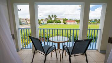 A balcony with a round table and two chairs, overlooking a green lawn and buildings.