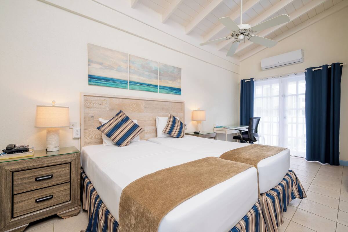 A hotel room with two beds, a desk, and a chair. There is a ceiling fan and an air conditioning unit.
