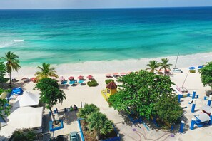 A beach with palm trees, umbrellas, and a lifeguard tower. - Time Out Hotel (St. Lawrence Gap)