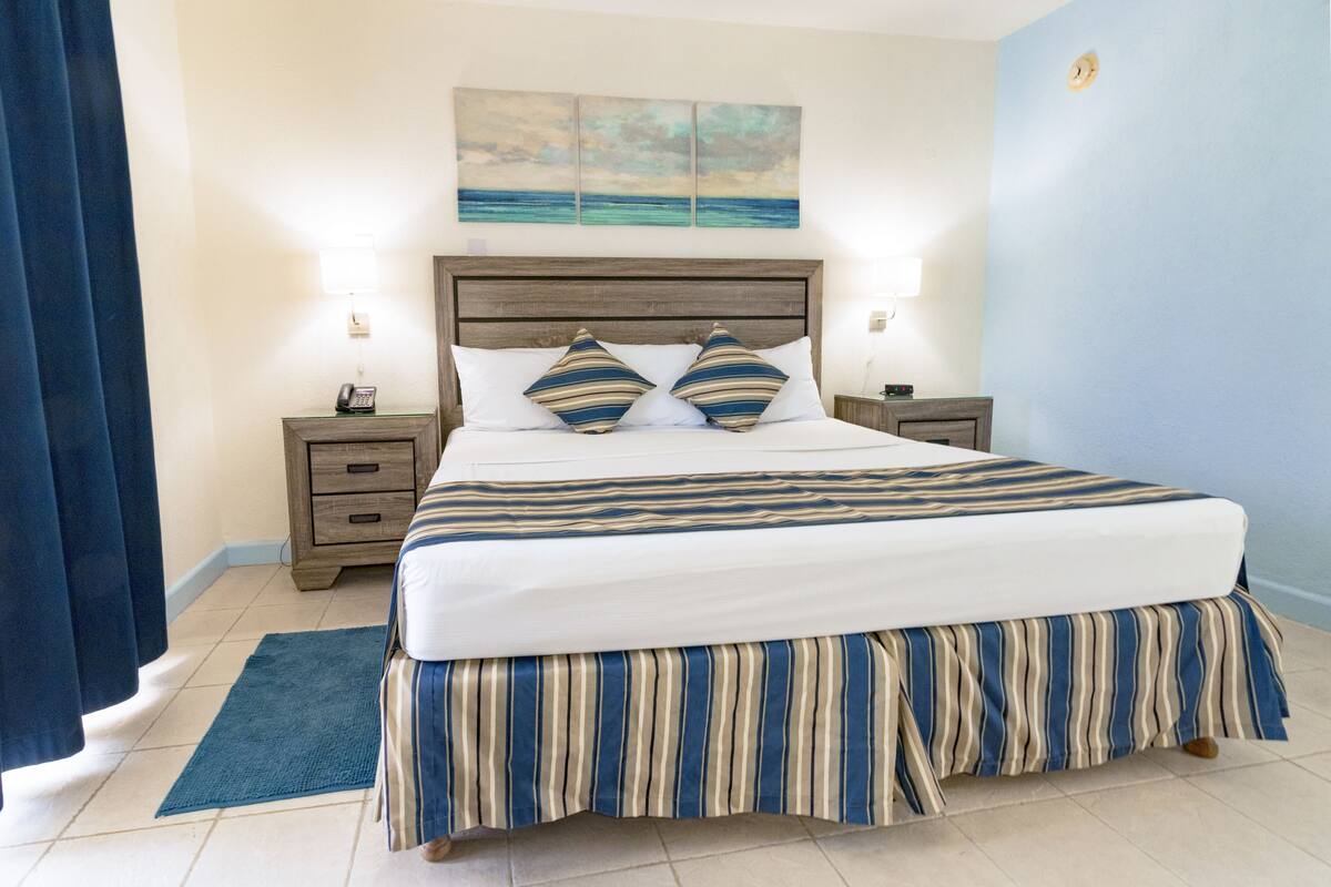 A neatly made bed with striped bedding, a wooden headboard, and a blue accent wall.