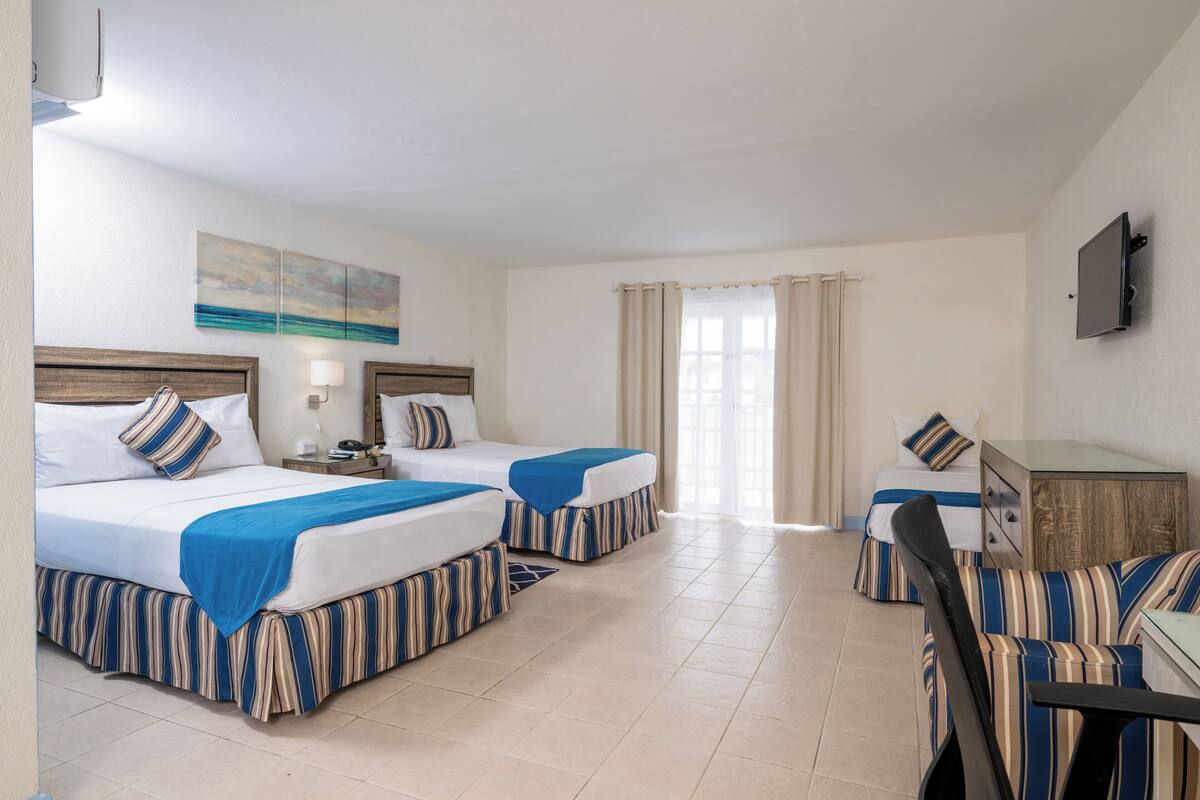 A hotel room with two beds, a desk, a chair, a TV, and a window with curtains.