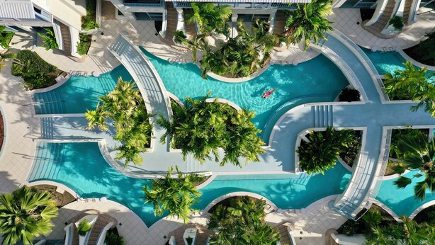Vue aérienne d’un complexe hôtelier doté de plusieurs piscines, de palmiers et d’une architecture moderne.