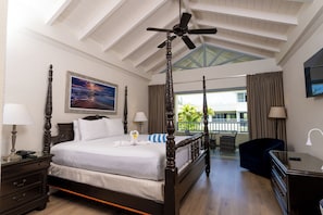 A four-poster bed with a ceiling fan, a painting on the wall, a balcony with a view, and a desk with a lamp. - Savannah Beach Club Hotel (Hastings)