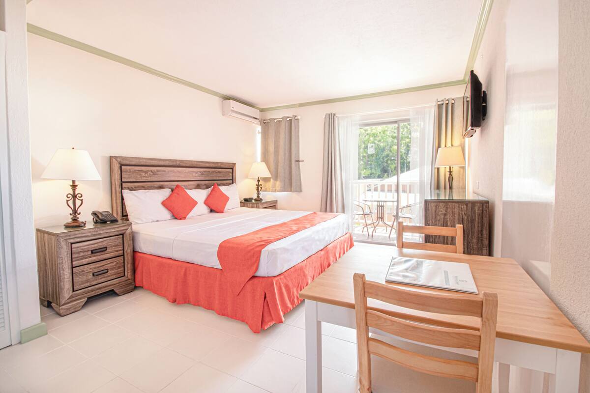 A hotel room with a bed, bedside tables, a desk, chairs, and a TV.