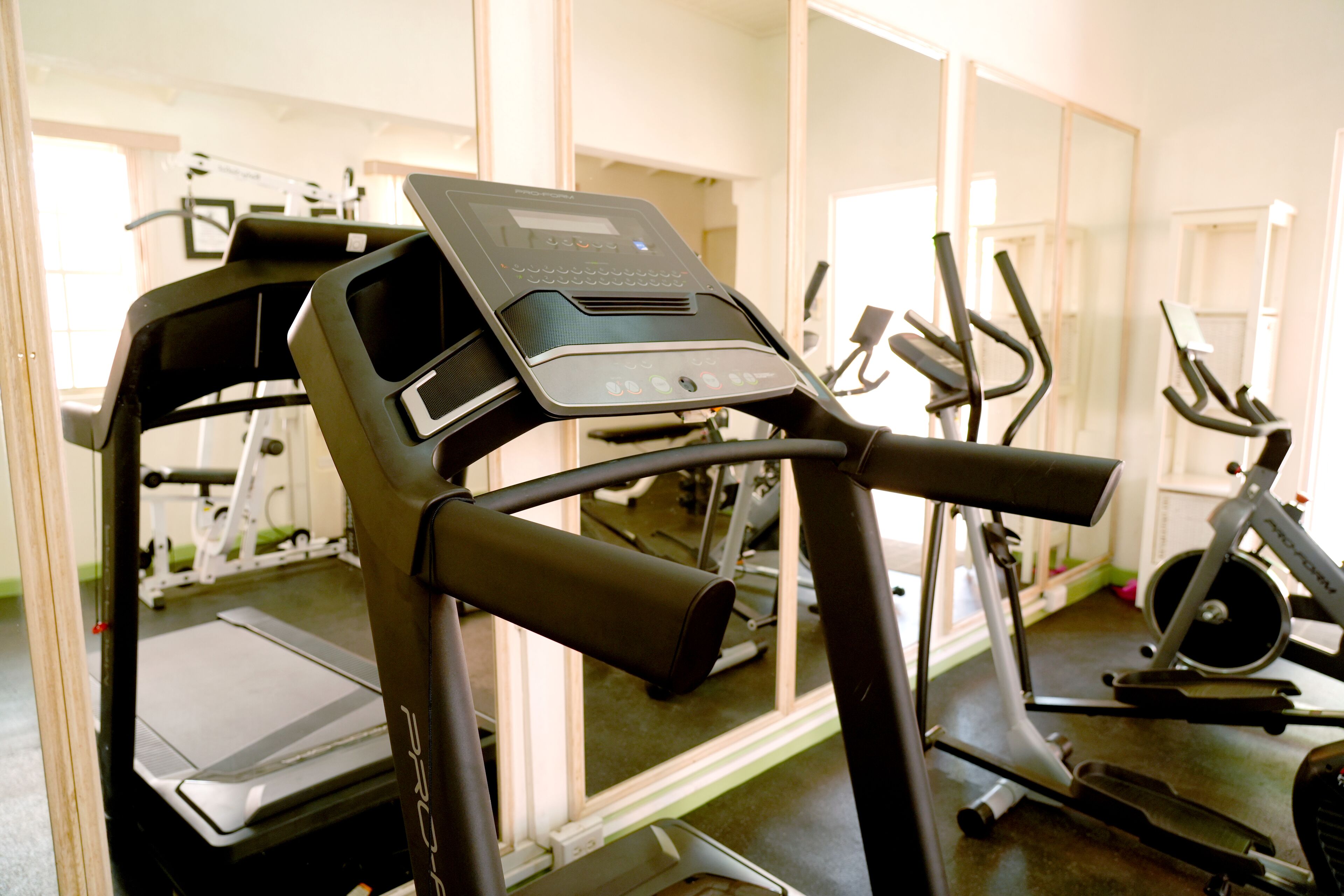 A gym with exercise equipment, including treadmills and stationary bikes, and a mirrored wall.