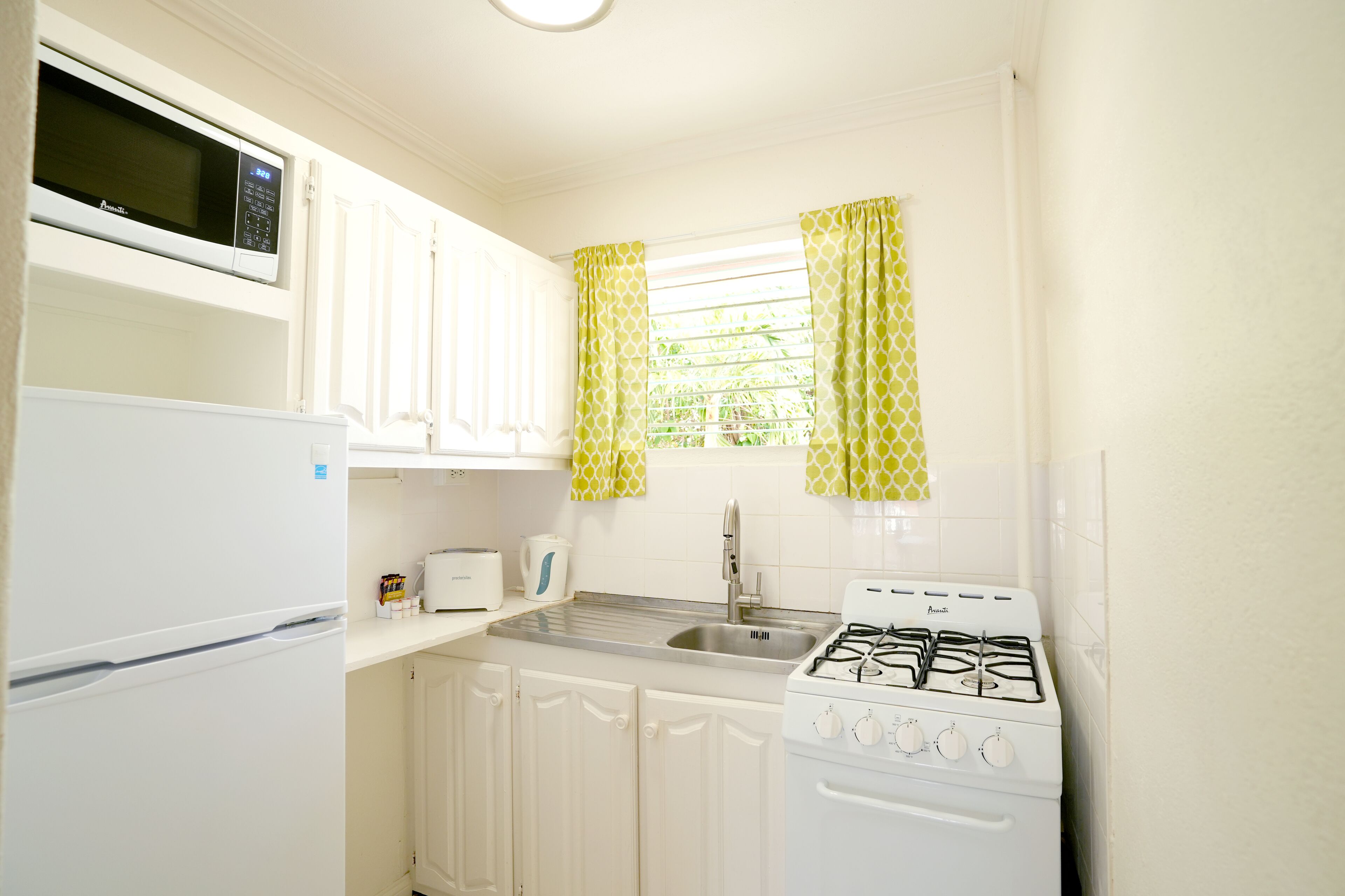 A compact kitchen with white appliances, a sink, and patterned curtains.
