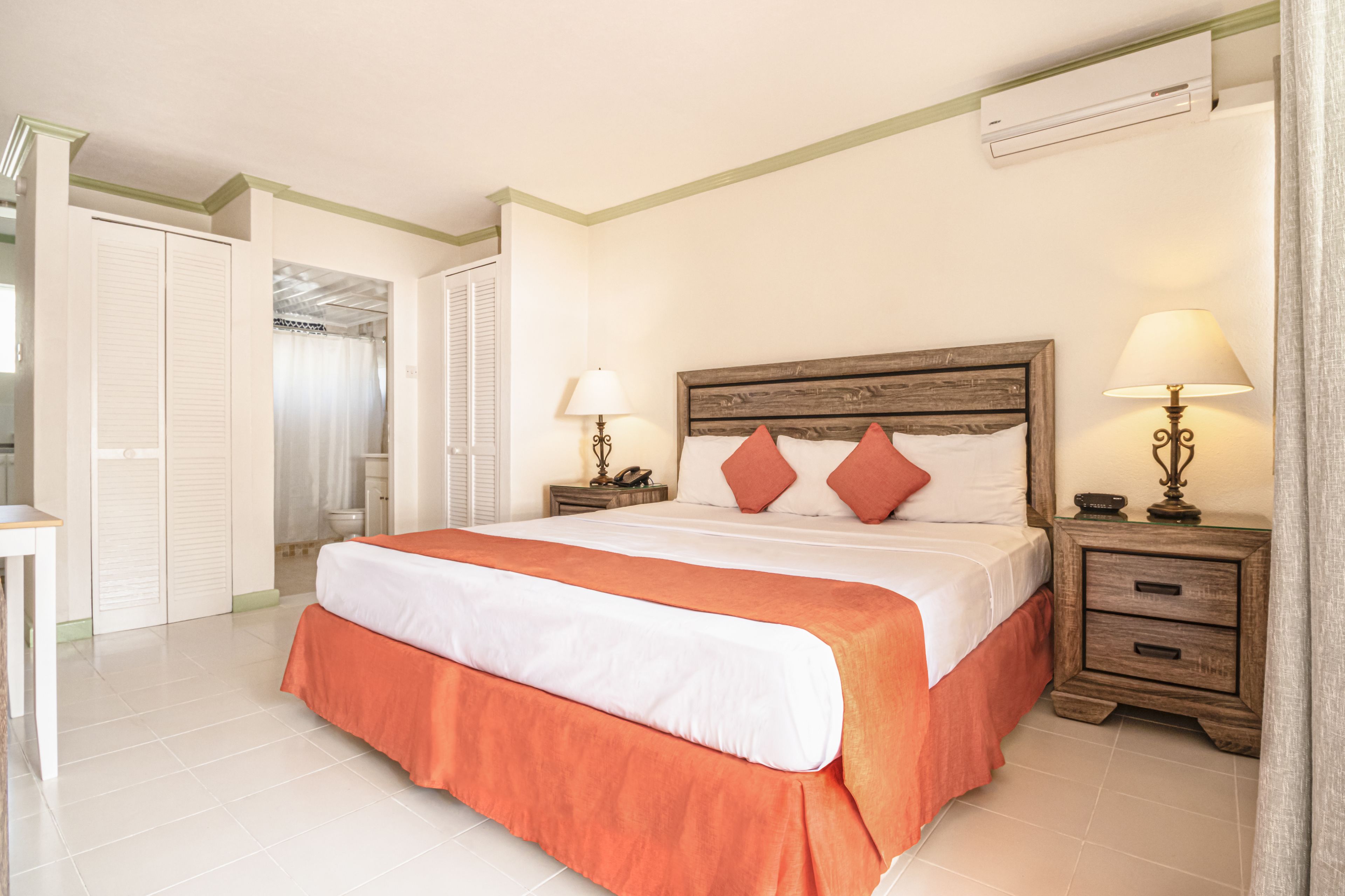 Una habitación de hotel con una cama grande, dos mesitas de noche con lámparas, un armario y un equipo de aire acondicionado en la pared.