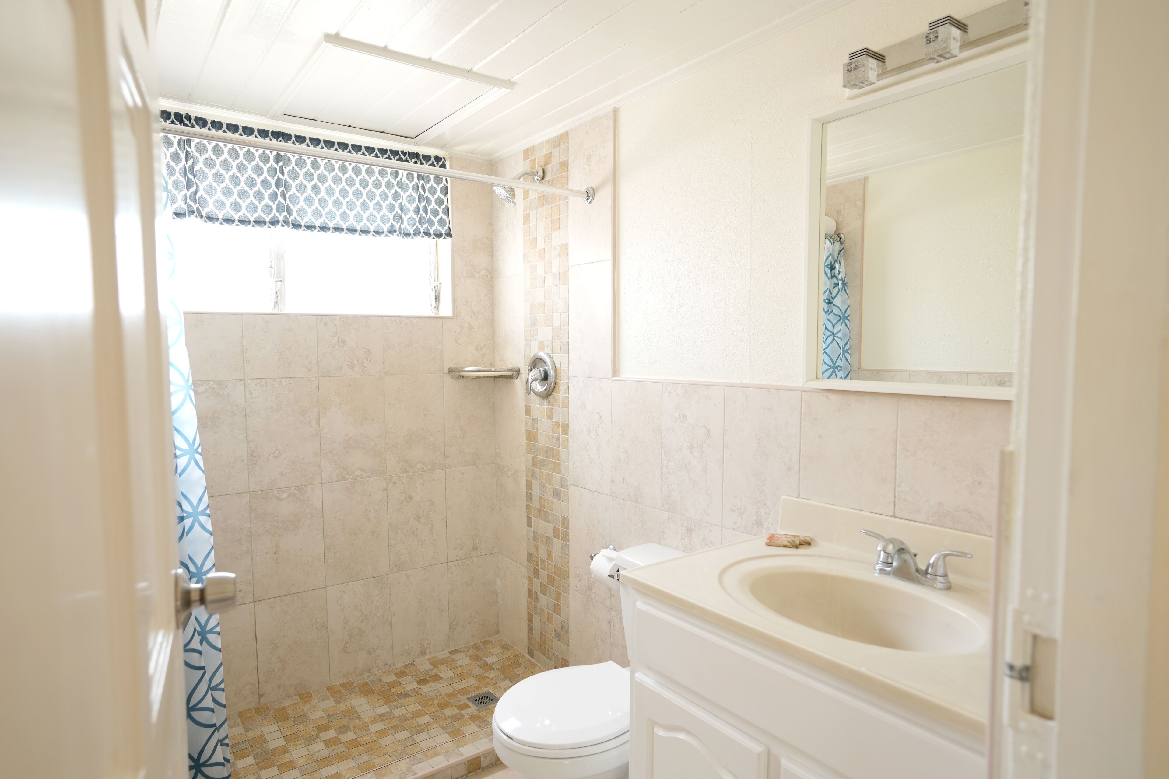 Un baño con ducha, inodoro, lavamanos y espejo.