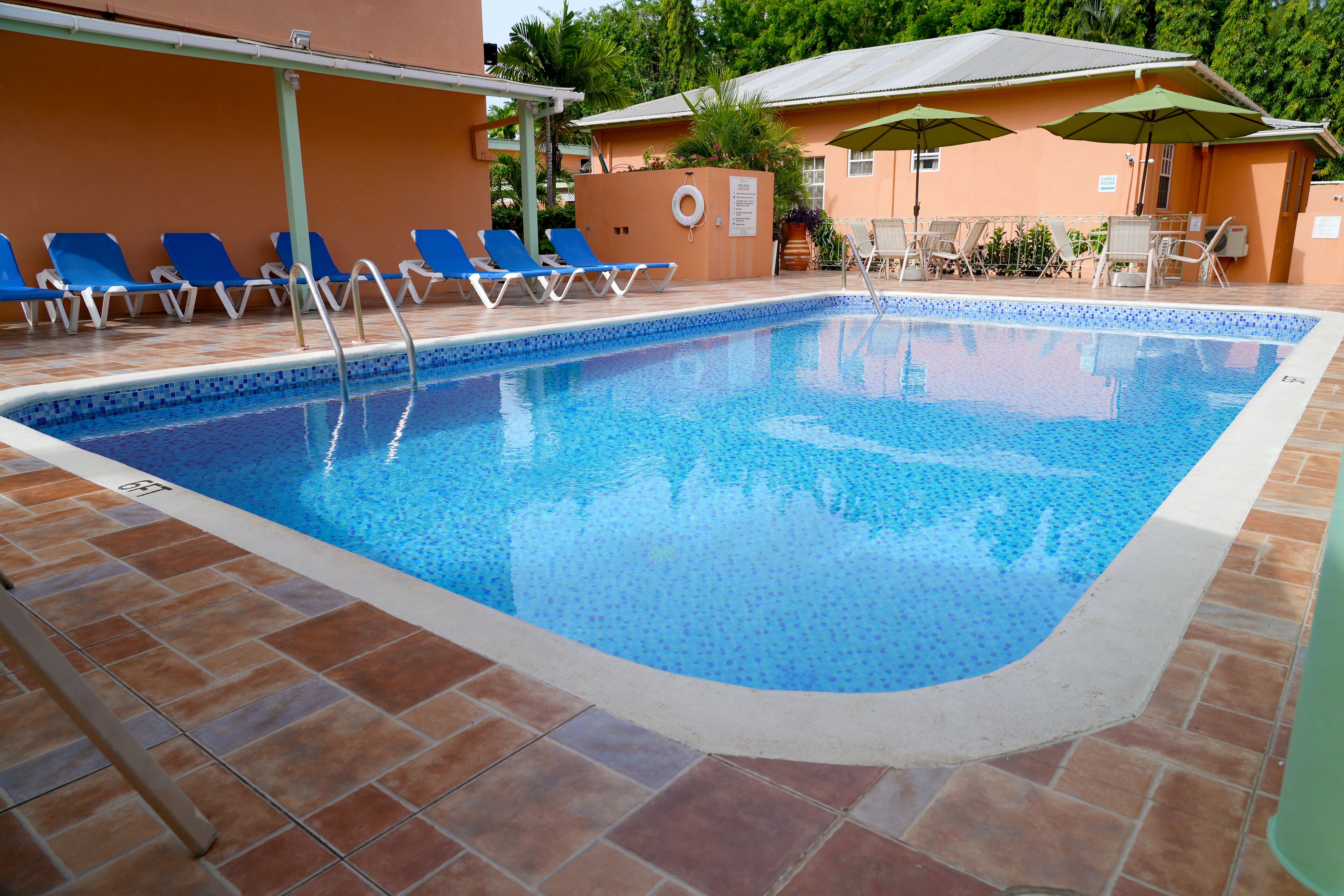 Una piscina con azulejos azules, un suelo de baldosas y sillas de descanso.