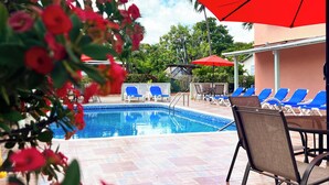 A pool area with blue lounge chairs and red umbrellas, surrounded by a tiled patio. - Worthing Court Apartment Hotel (Worthing)