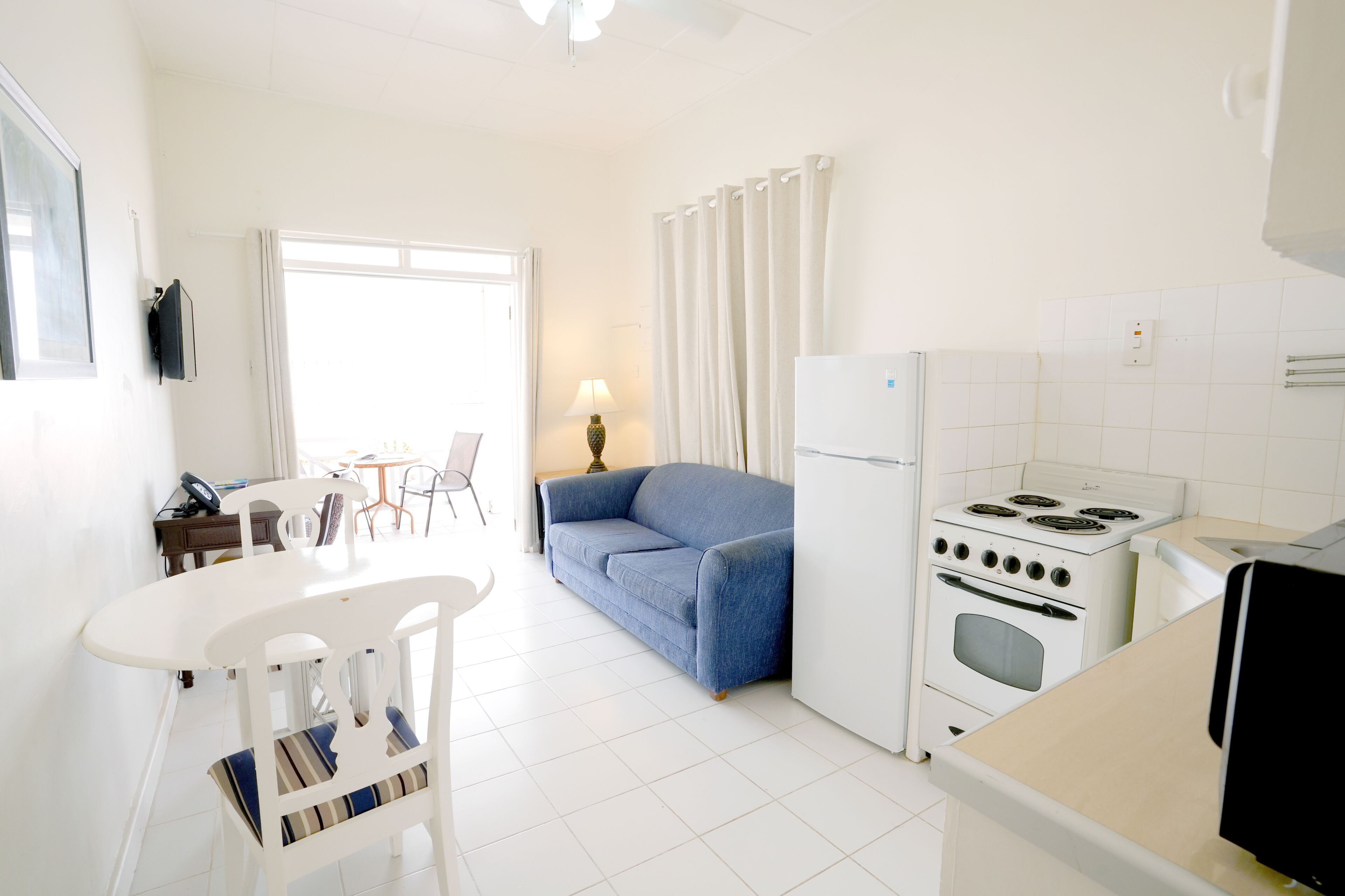 Une cuisine avec des appareils électroménagers blancs, une table à manger avec des chaises, un canapé et une lampe.