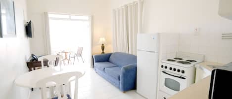 Una cocina con electrodomésticos blancos, una mesa de comedor con sillas, un sofá y una lámpara.