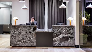 Uma área de recepção moderna com balcões de mármore, iluminação pendente e uma grande janela com cortinas.
