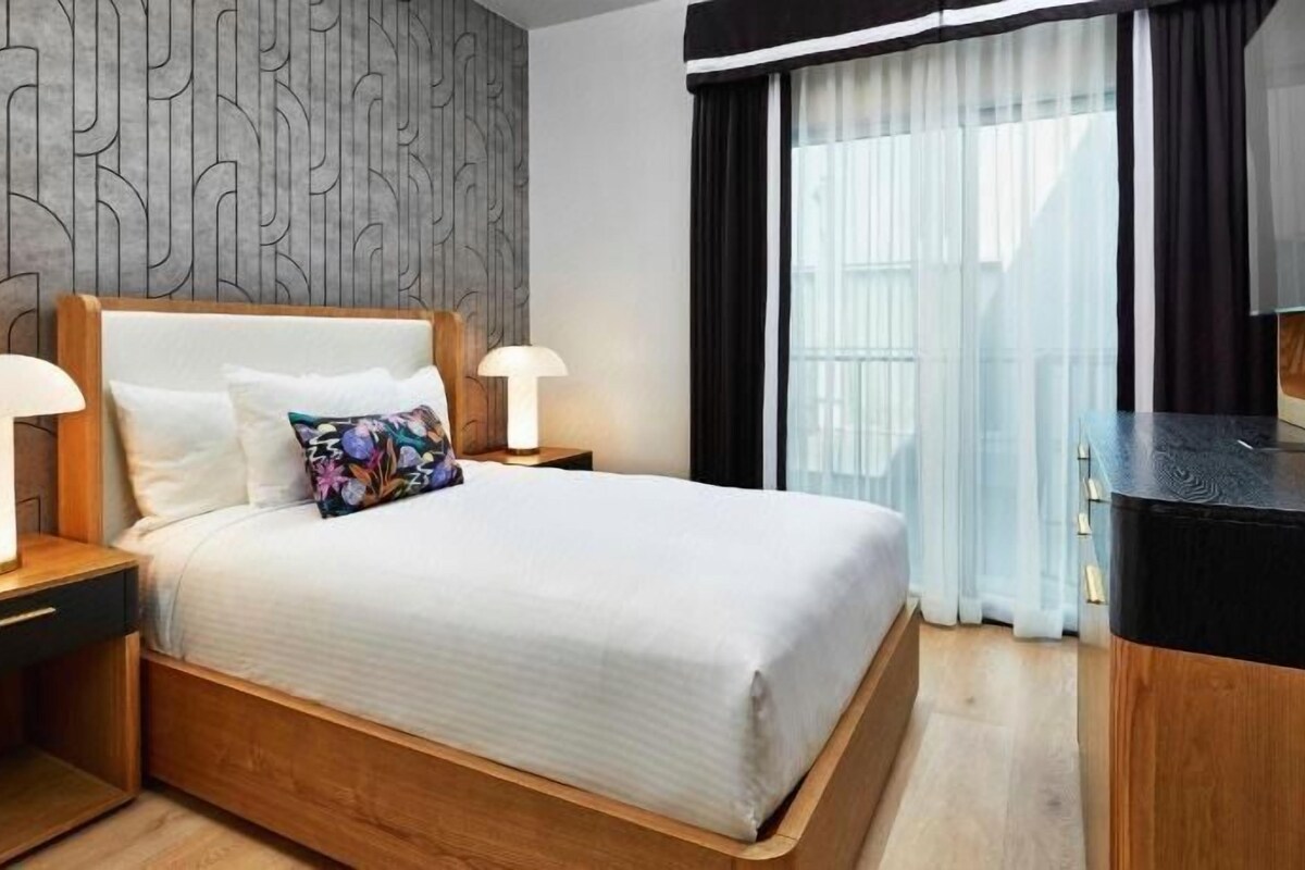 A hotel room with a bed, nightstands, a TV, and a view of the outdoors.