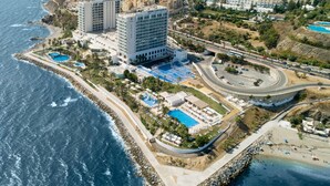 Un hotel frente al mar con varias piscinas, una carretera y una playa.