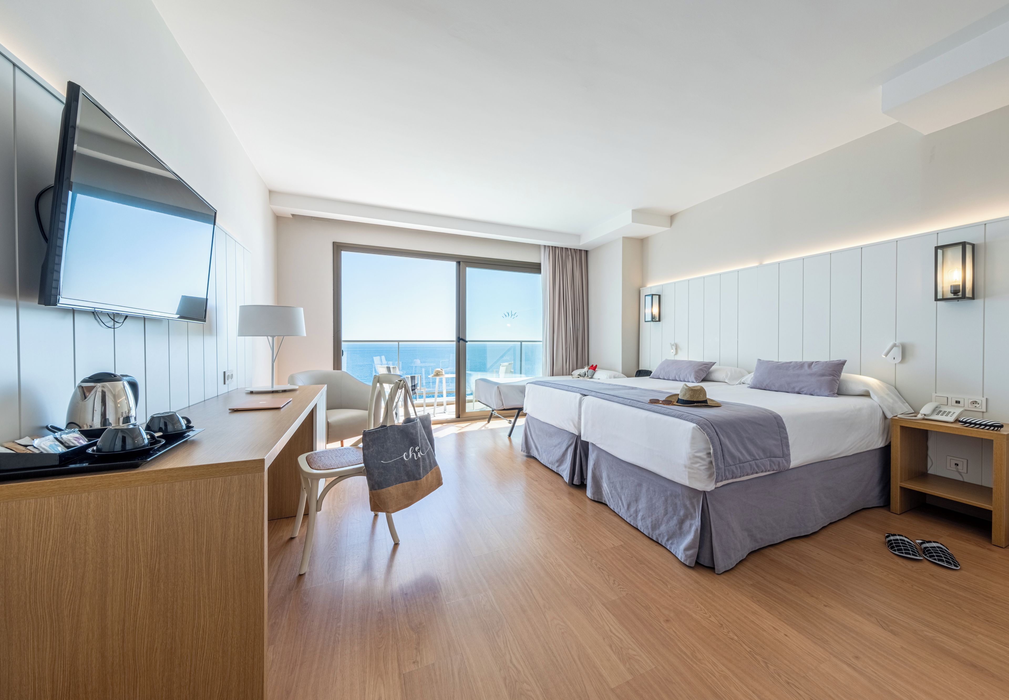A modern hotel room with a large bed, a desk, a TV, and a balcony with a view.