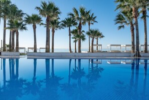A clear blue pool with palm trees and lounge chairs, surrounded by a white poolside area. - Estival Torrequebrada (Benalmádena)