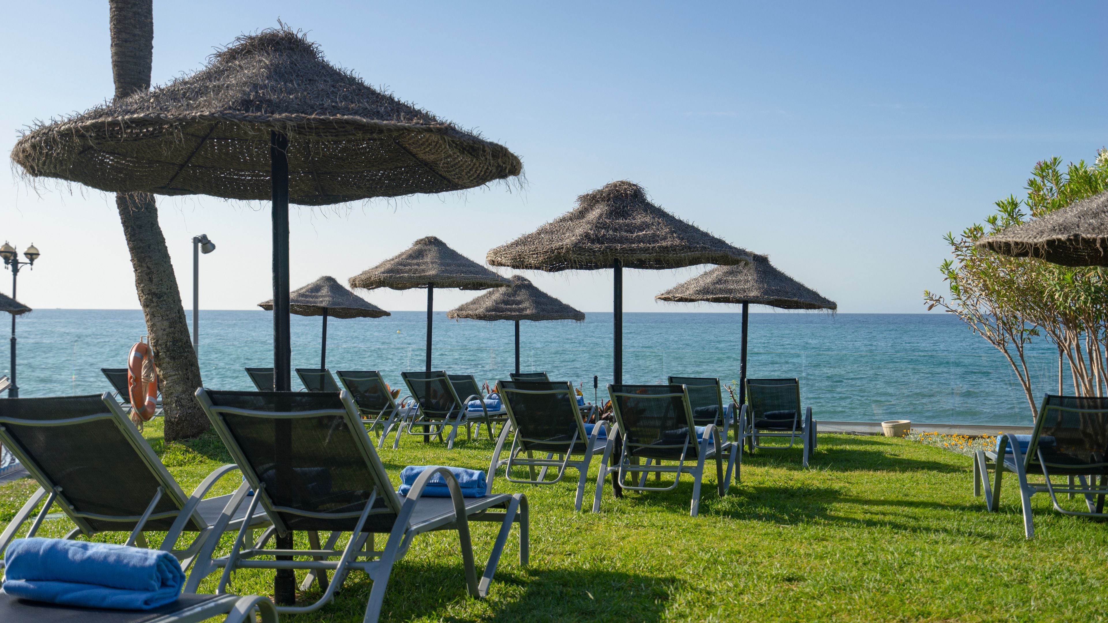 A beachside lounge with thatched umbrellas and lounge chairs facing the sea.