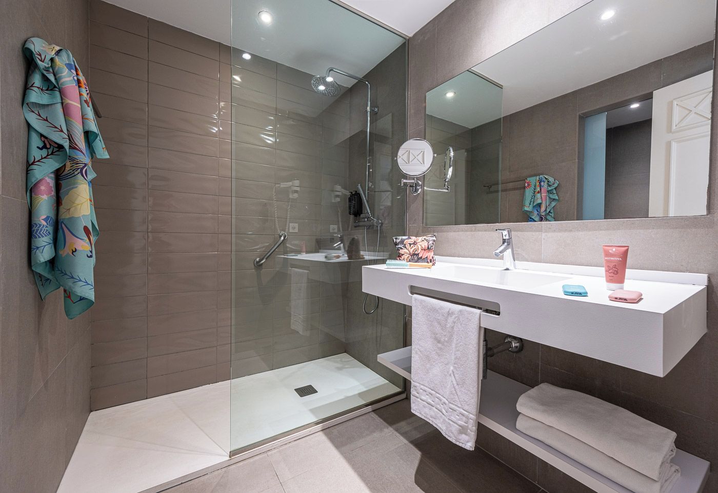 Une salle de bain moderne dotée d’une douche à parois de verre, d’un meuble-lavabo blanc avec un miroir et d’un porte-serviettes orné de serviettes colorées.