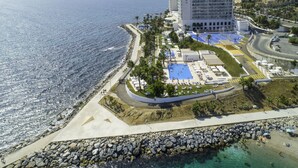 An aerial view of a coastal hotel with a pool area, a beach, and a rocky shoreline.