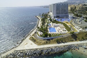 An aerial view of a coastal hotel with a pool area, a beach, and a rocky shoreline.