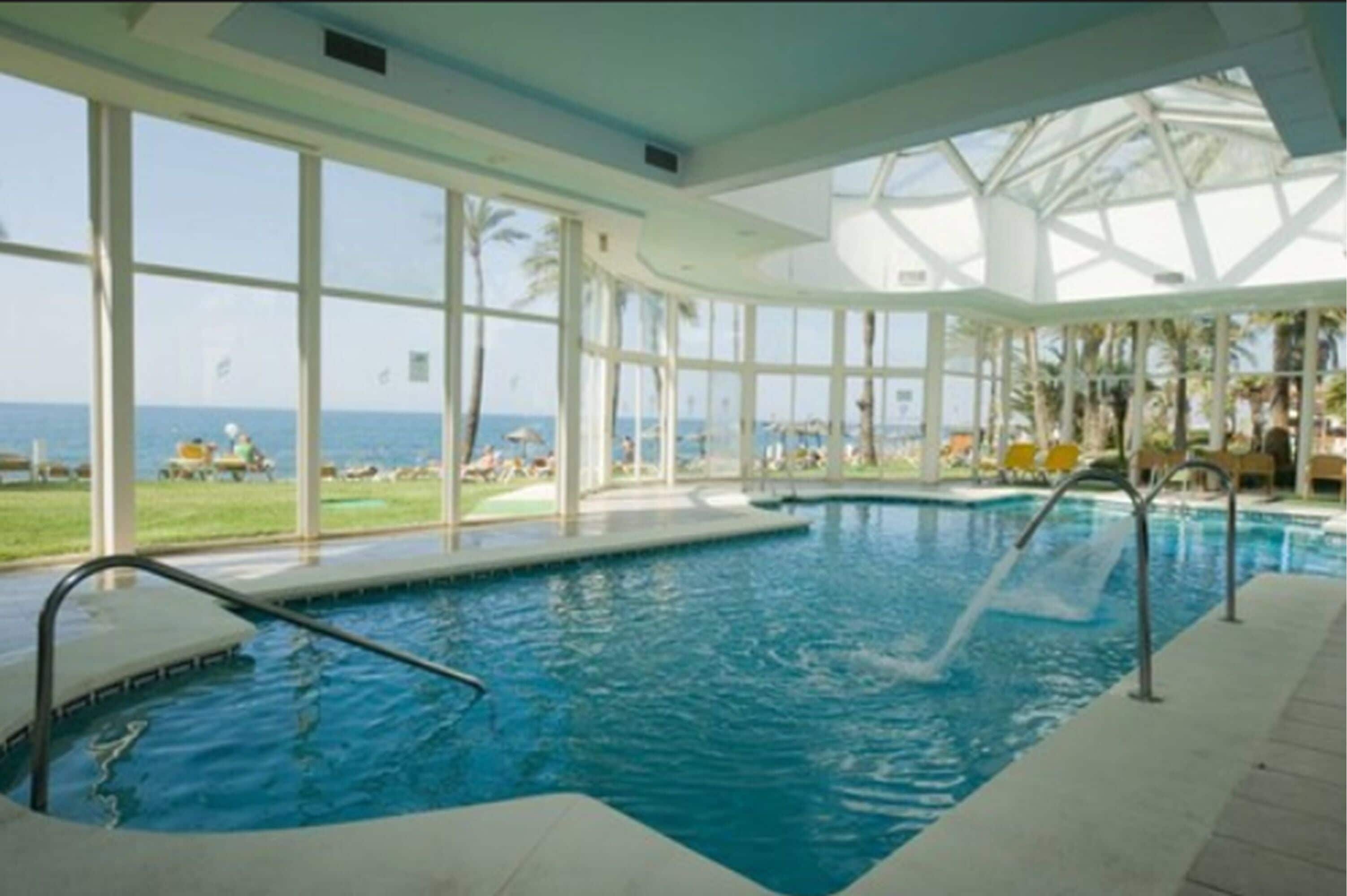 An indoor swimming pool with clear views of the ocean through large windows.
