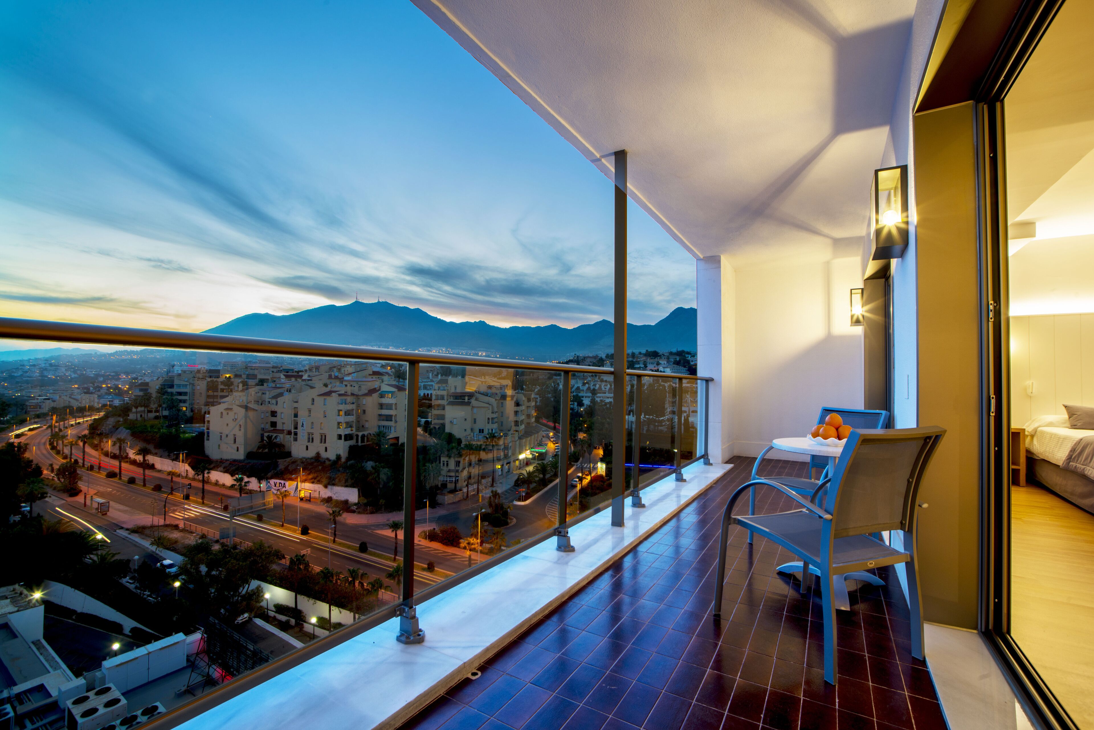 A balcony with a city view, a table with chairs, and a bed in the adjacent room.