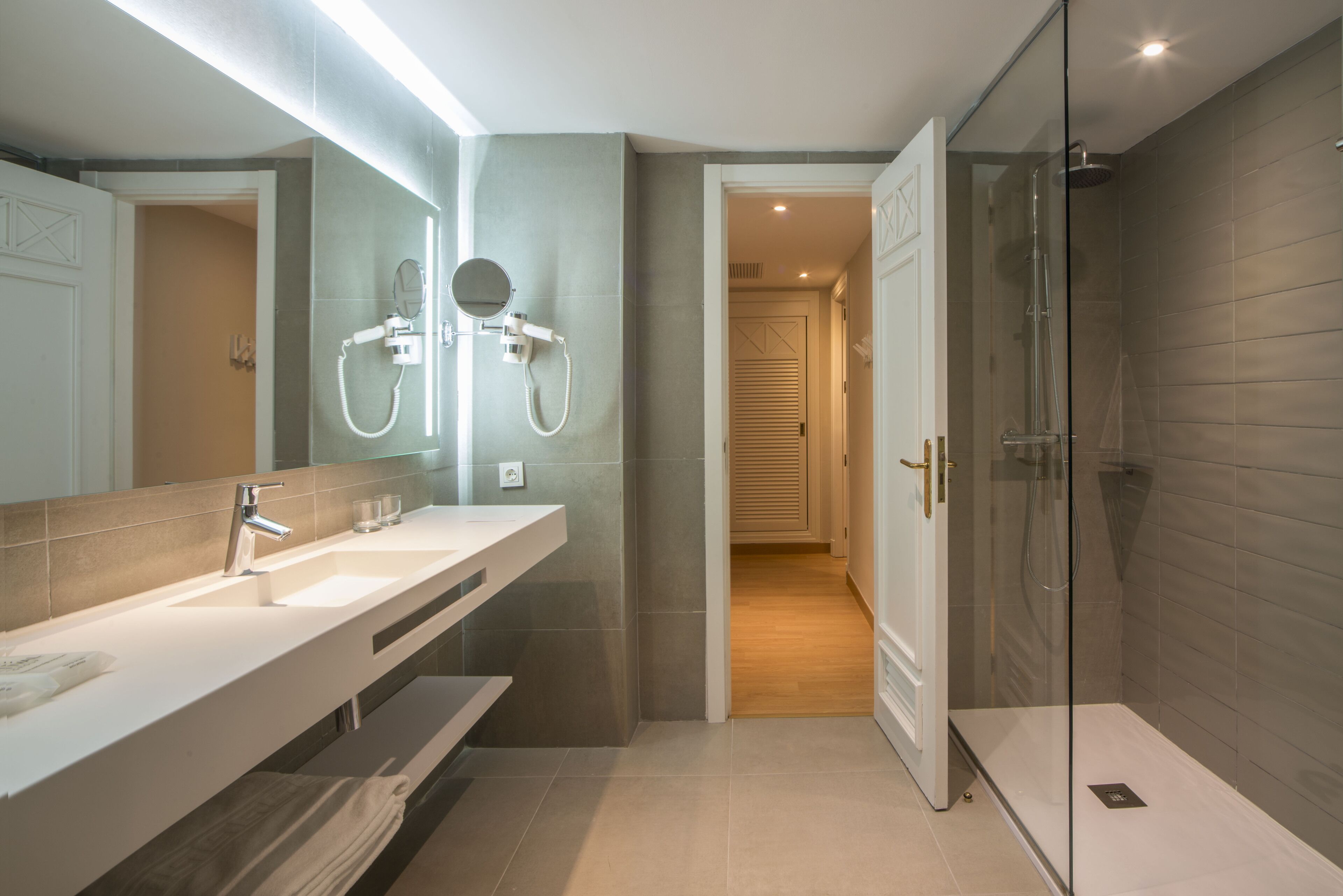 A modern bathroom with a large mirror, two sinks, a shower, and a walk-in shower.