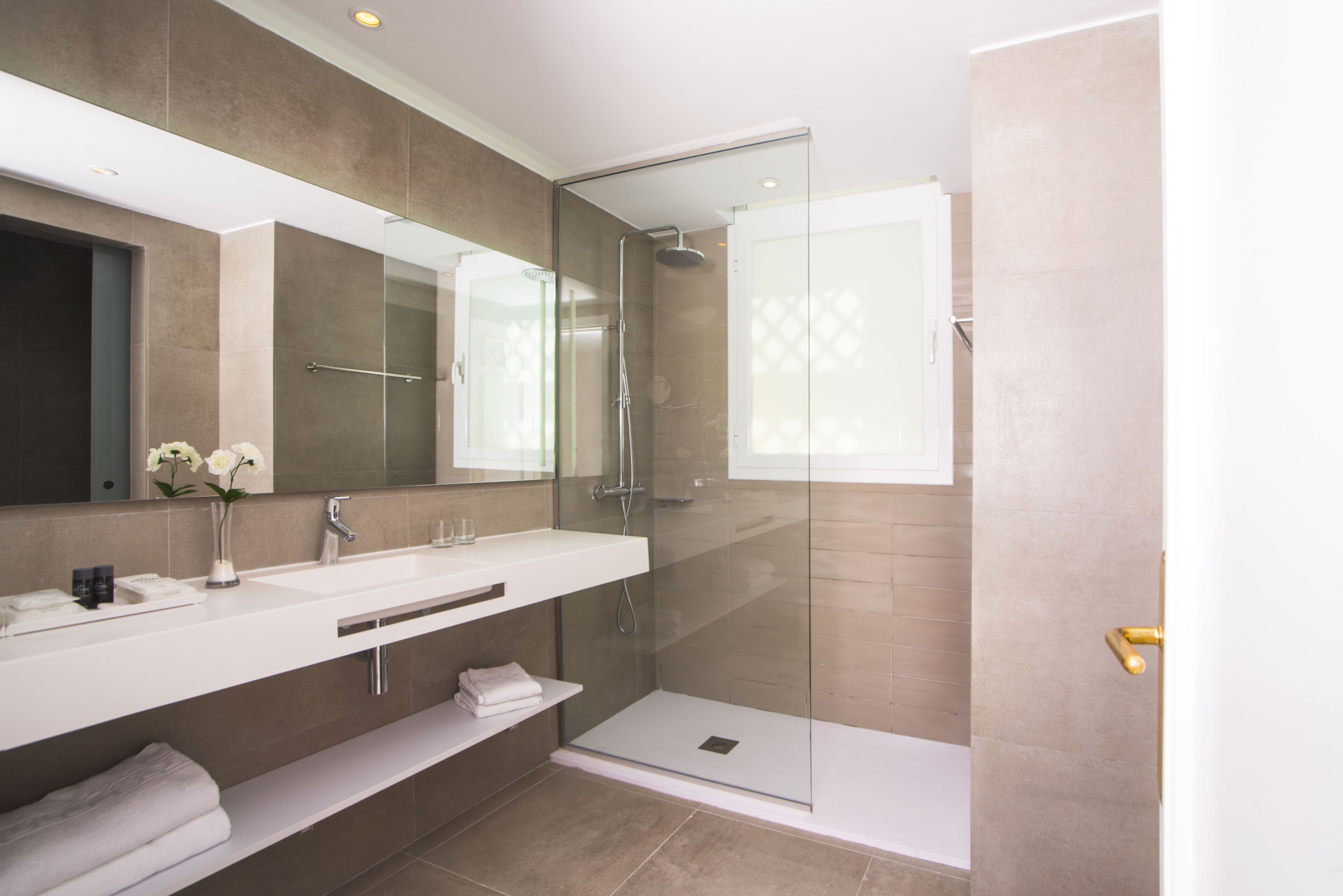 Un baño moderno con ducha de vidrio, un espejo grande y un tocador blanco.