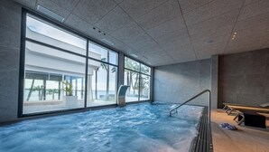 Una gran piscina interior con vistas al océano, una tumbona y un pequeño rincón de descanso.