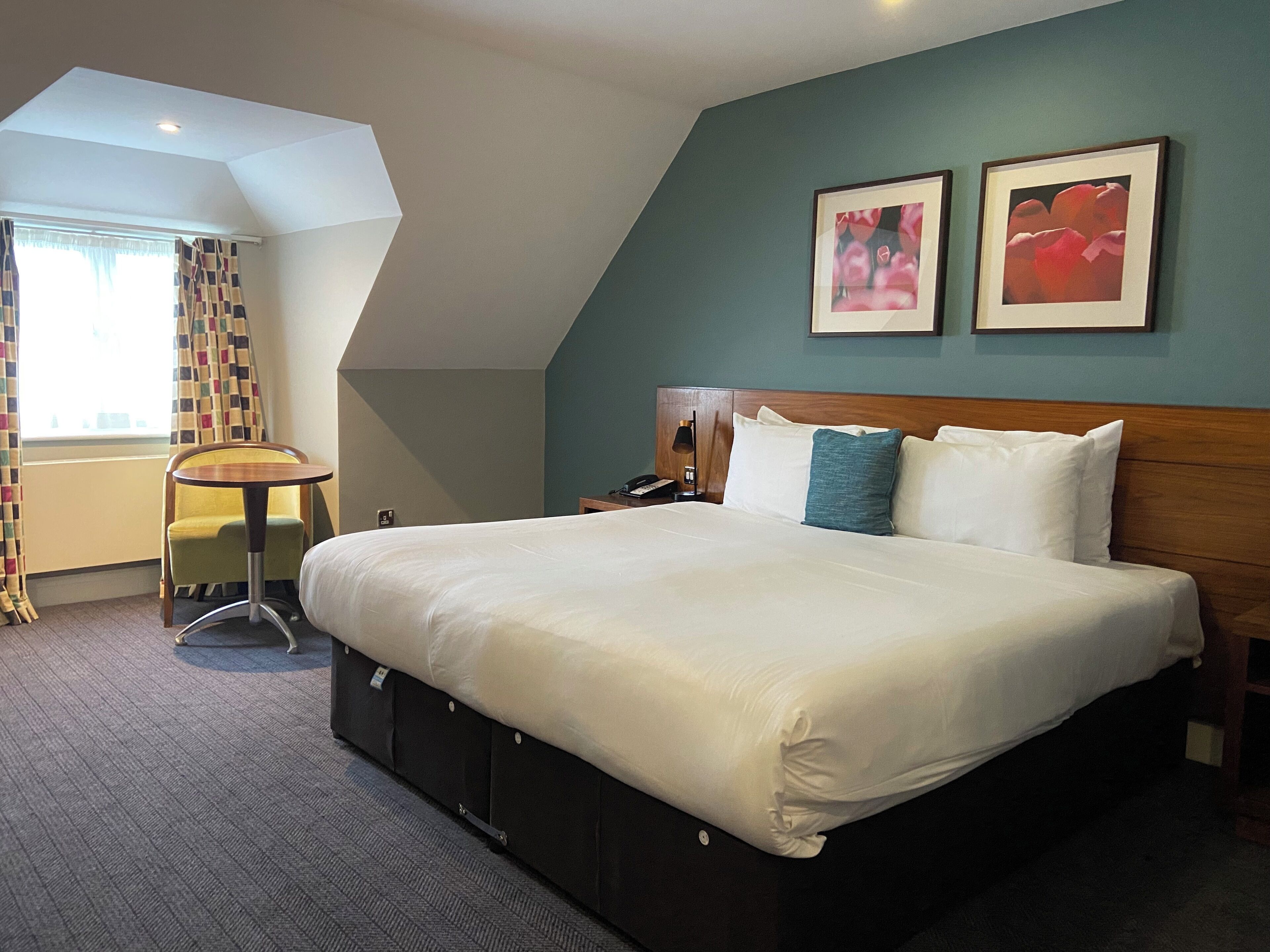 A hotel room with a large bed, a desk, and two framed pictures on the wall.
