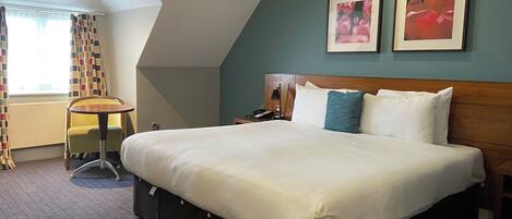 A hotel room with a large bed, a desk, and two framed pictures on the wall.