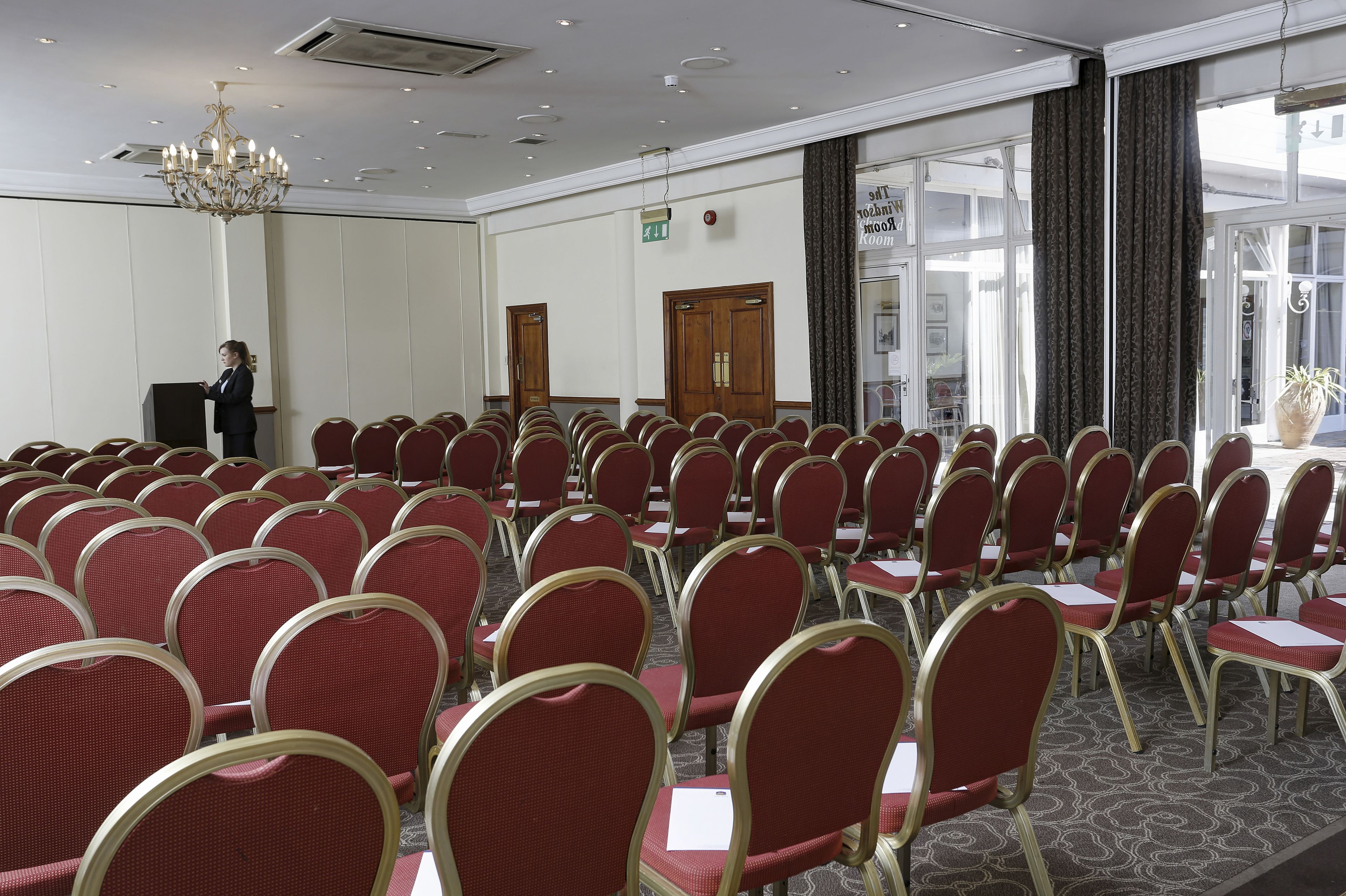 A conference room with rows of red chairs, a podium, and a chandelier.