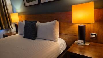A hotel room with a bed, two bedside lamps, a nightstand, and a wall-mounted switch.