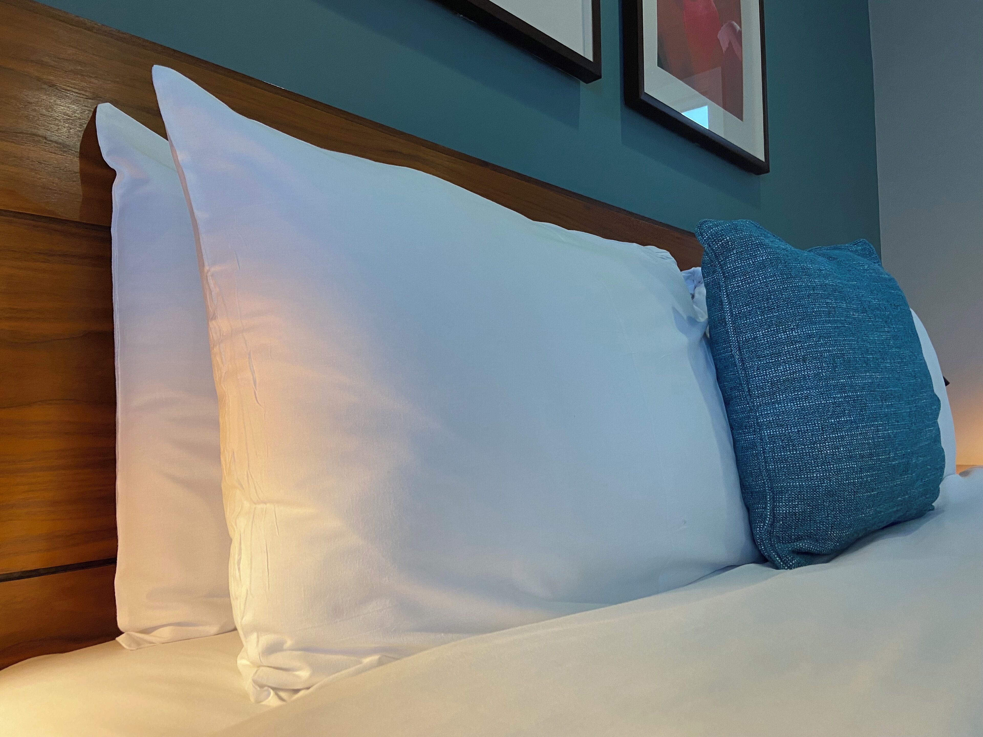 A bed with white and blue pillows, wooden headboard, and a teal wall with framed pictures.