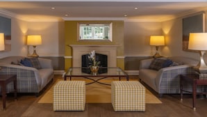 A living room with two sofas, a glass coffee table, and a fireplace. There are two lamps on either side of the room. - Best Western Ship Hotel (Weybridge)