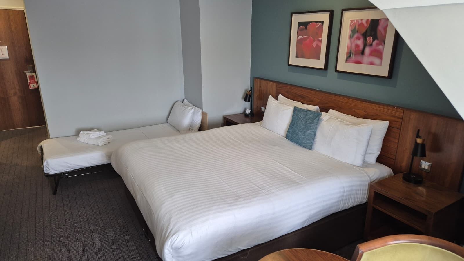 A hotel room with a large bed, a bedside table, a chair, and a small desk.