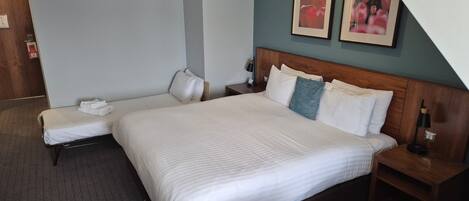 A hotel room with a large bed, a bedside table, a chair, and a small desk.