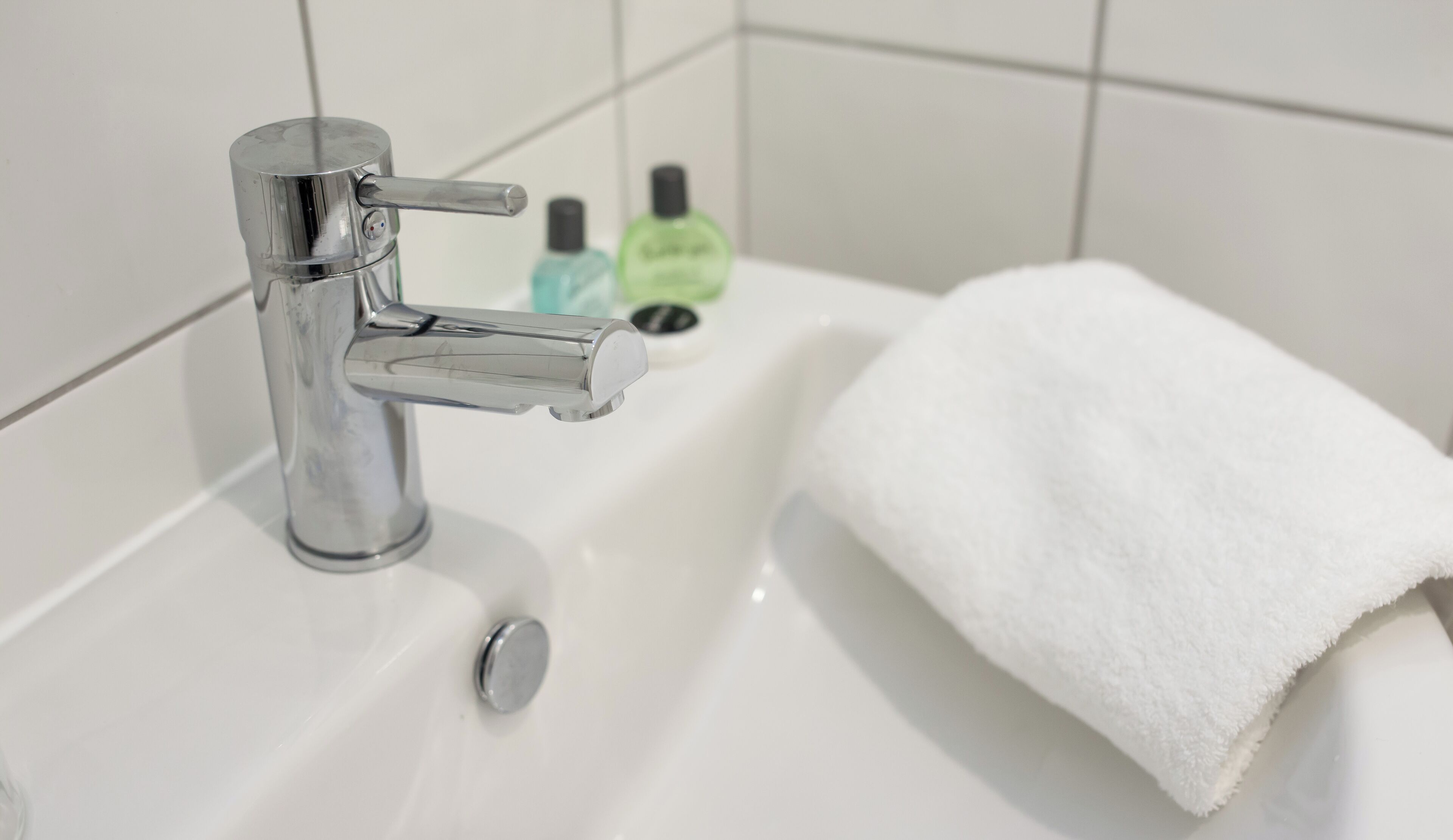 A bathroom with a chrome faucet, a white sink, and a white towel.