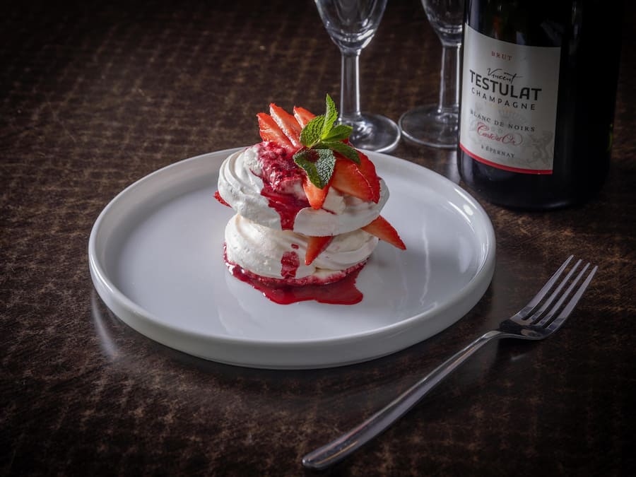 A dessert on a plate with a bottle of Brut Testulat Champagne in the background.