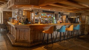 A bar area with a wooden bar counter, multiple stools, and a variety of bottles and glasses. - Best Western Ship Hotel (Weybridge)