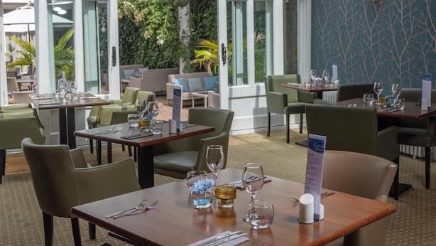 A restaurant with tables set for dining, a menu stand, and a view of greenery outside. - Best Western Ship Hotel (Weybridge)