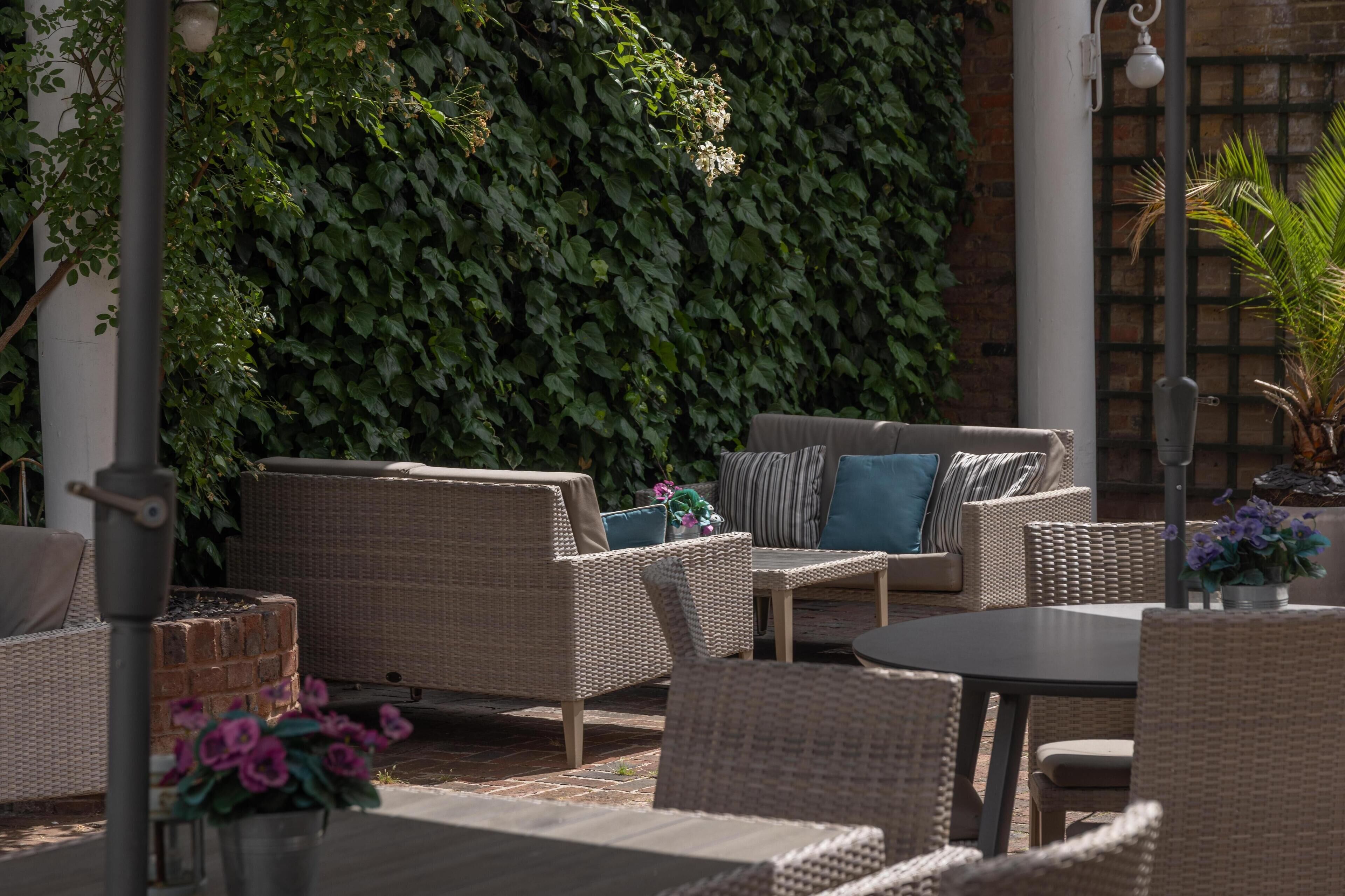 An outdoor seating area with wicker furniture, a brick wall, and a potted plant.