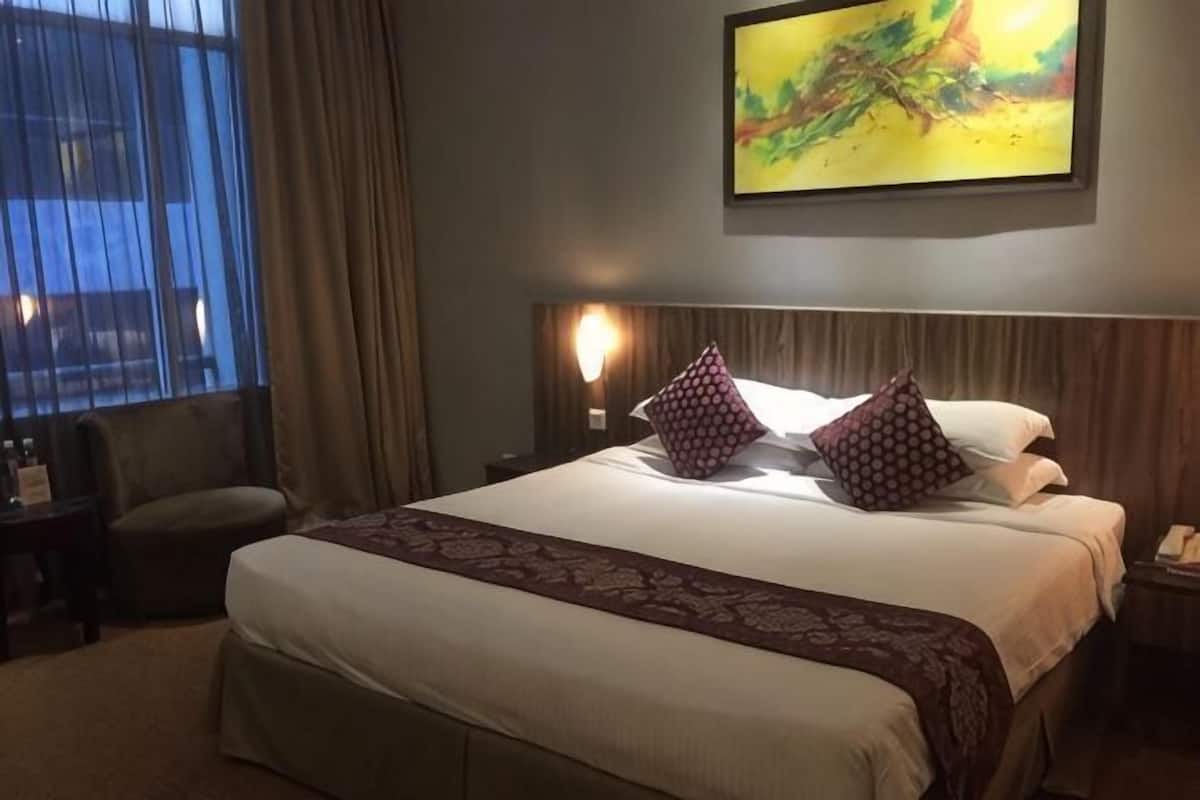 Une chambre d’hôtel avec un grand lit, une table de chevet, une chaise, un tableau au mur et une fenêtre avec des rideaux.