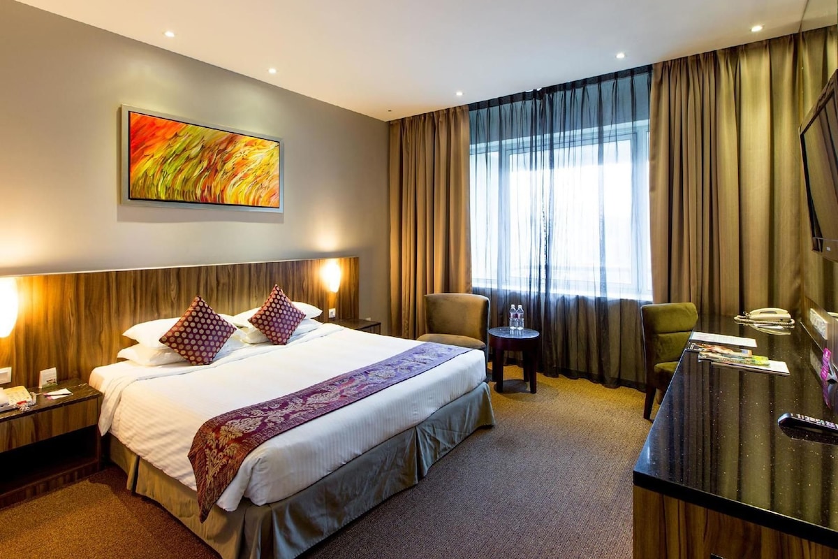 Une chambre d’hôtel avec un grand lit, un bureau, une chaise, une petite table et un tableau au mur.