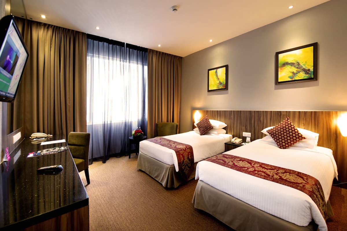 Habitación de hotel con dos camas, un escritorio con ordenador, televisión y ventana con cortinas.