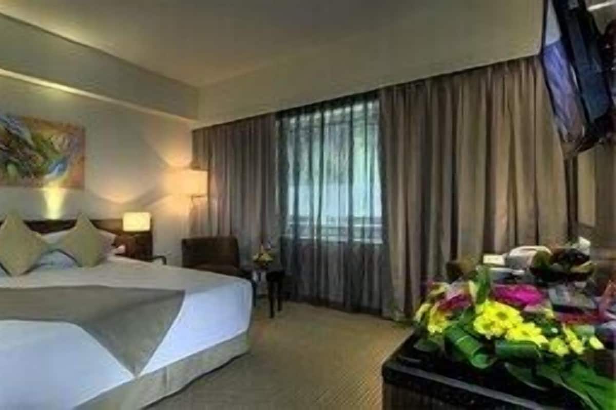 Una habitación de hotel con una cama grande, dos mesitas de noche, un televisor y un arreglo floral, además de un cuadro en la pared.