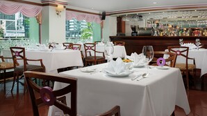 A restaurant with tables set for dining, chairs, and a bar area with bottles and glasses. - Hotel Sintra (Macau)