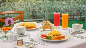 A breakfast setting with a variety of dishes, including eggs, toast, and fruit, on a table with a view of greenery and buildings in the background. - Hotel Sintra (Macau)